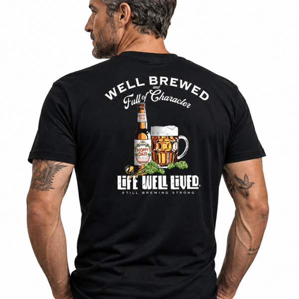 A man shown from the back wearing a black graphic t-shirt. The shirt features a large back print with the text 'WELL BREWED Full of Character' and 'LEFT WELL LIVED THE BREWING WAY' surrounding an illustration of a beer bottle, a beer mug, and hops.