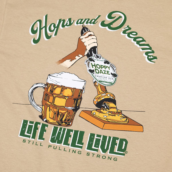 This mens graphic back print Tee shirt, shows an image of a beer pump being pulled, next to the pump is a traditional pint glass full of beer, the beer being pulled is called 'Hoppy Daze' The strapline above says hops & Dreams, a great t shirt for any beer lover, finished in golden graphics with green lettering on a Tan colour base Tee.