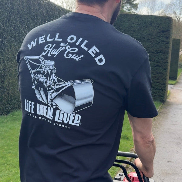 Black Well Oiled Half Cut T‑Shirt with bold lawnmower back print worn outdoors.