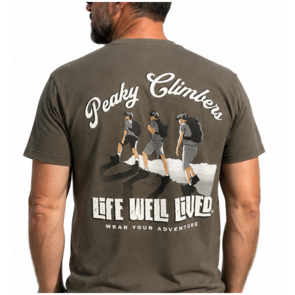 A man wearing a dark olive green t-shirt from the back, featuring a large graphic print of three climbers and the text 'Peaky Climbers' and 'LIFE WELL LIVED'.
