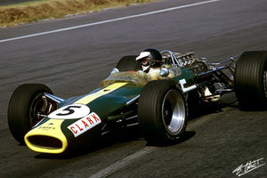 Old formula one lotus race car, driven by Jim Clarke driving through a corner at speed. The car is british racing green with yellow bonnet stripe.