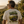 A man wearing a cream-colored t-shirt with a large green and brown graphic on the back, standing in an outdoor vineyard at sunset.