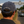 A man viewed from behind wearing a navy blue baseball cap with 'Life Well Lived' embroidered in white on the back, standing at Goodwood Racecourse with vintage race cars and the Goodwood Arch in the background.