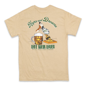 This mens graphic back print Tee shirt, shows an image of a beer pump being pulled, next to the pump is a traditional pint glass full of beer, the beer being pulled is called 'Hoppy Daze'  The strapline above says hops & Dreams, a great t shirt for any beer lover, finished in golden graphics with green lettering on a Tan colour base Tee.