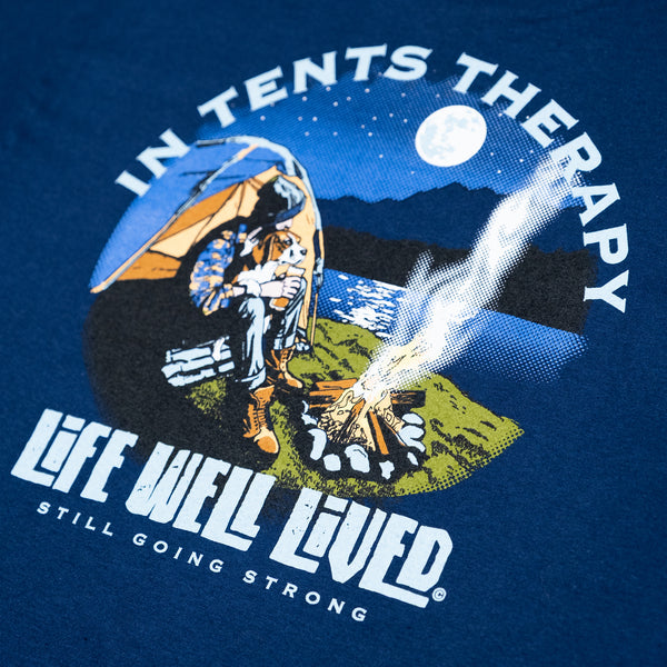  Stunning Navy blue T shirt, a back printed  Camping themed design T shirt, there is a man sat in the moonlight over a lake, he is sat with his dog snug on his lap in his tent. He has a campfire burning in front of him and a beer in his hand. The smoke from the campfire is drifting up over the lake in front of a full moon, The image is in a circular style and located in the middle of the T shirt. the strapline says 'In Tents Therapy' and blow is the brand logo 'Life Well Lived',  small logo on front chest.