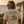 A man standing on a beach path at sunset, viewed from behind, wearing a cream-colored t-shirt with a dark brown graphic that reads 'LORD SEAS' and 'LIFE WELL LOVED'. A surfboard leans against a cliff in the background.