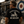 A man wearing a black graphic t-shirt with a retro scooter design and the text 'MODOPHENIA' and 'LIFE WELL LOVED' is shown from behind, standing next to a vintage white scooter in front of a cafe with a target mural.