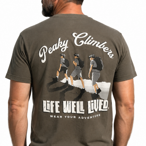 A man wearing a dark olive green t-shirt from the back, featuring a large graphic print of three climbers and the text 'Peaky Climbers' and 'LIFE WELL LIVED'.