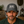 A man wearing a dark gray washed baseball cap with a white patch that reads 'LIFE WERE REWARDED' and a dark green t-shirt, photographed in a rustic indoor setting.