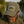 A man wearing an olive green baseball cap with a 'One Fishing and Away' embroidered patch, photographed outdoors by a lake with fishing rods in the background.