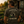 A man wearing a dark olive green graphic t-shirt stands in a garden, viewed from behind. The shirt features a large graphic of a small cabin with vegetables and the text 'GROW BIG Go Game LIFE WELL LIVED STILL GROWING STRONG'.