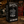 A black 20 oz Thermal Tumbler mug with a white graphic of a motorcycle and the text 'WELL OILED and Still Going Strong' displayed inside its branded black packaging box on a wooden workbench with a garage background.