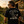 A man viewed from behind wearing a black graphic t-shirt with a large white and gray design on the back, standing in a backyard next to a lawnmower in front of a wooden shed.